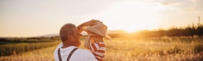 man putting cowboy hat on child that he is holding while standing in a field